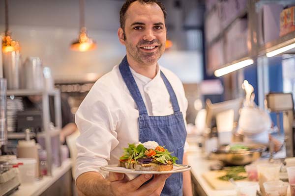 The chef Dominic Ansel holding out a plate of food for the camera.